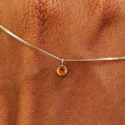 Close up view of a 14k champagne gold Fire Opal Necklace draped across the back of a model's hand