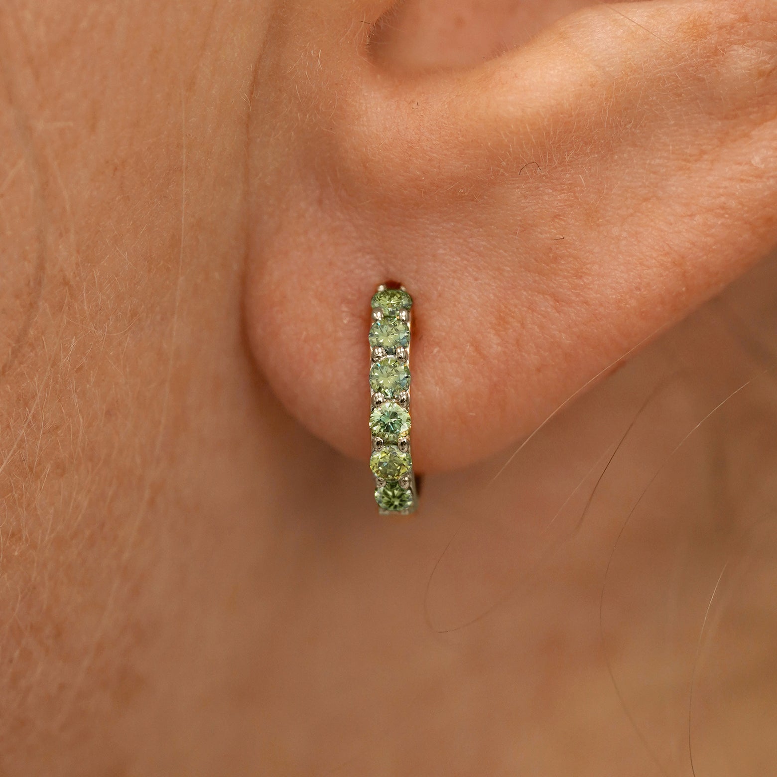 Close up view of a model's ear wearing a champagne gold Small Light Green Lab Diamond Huggie Hoop