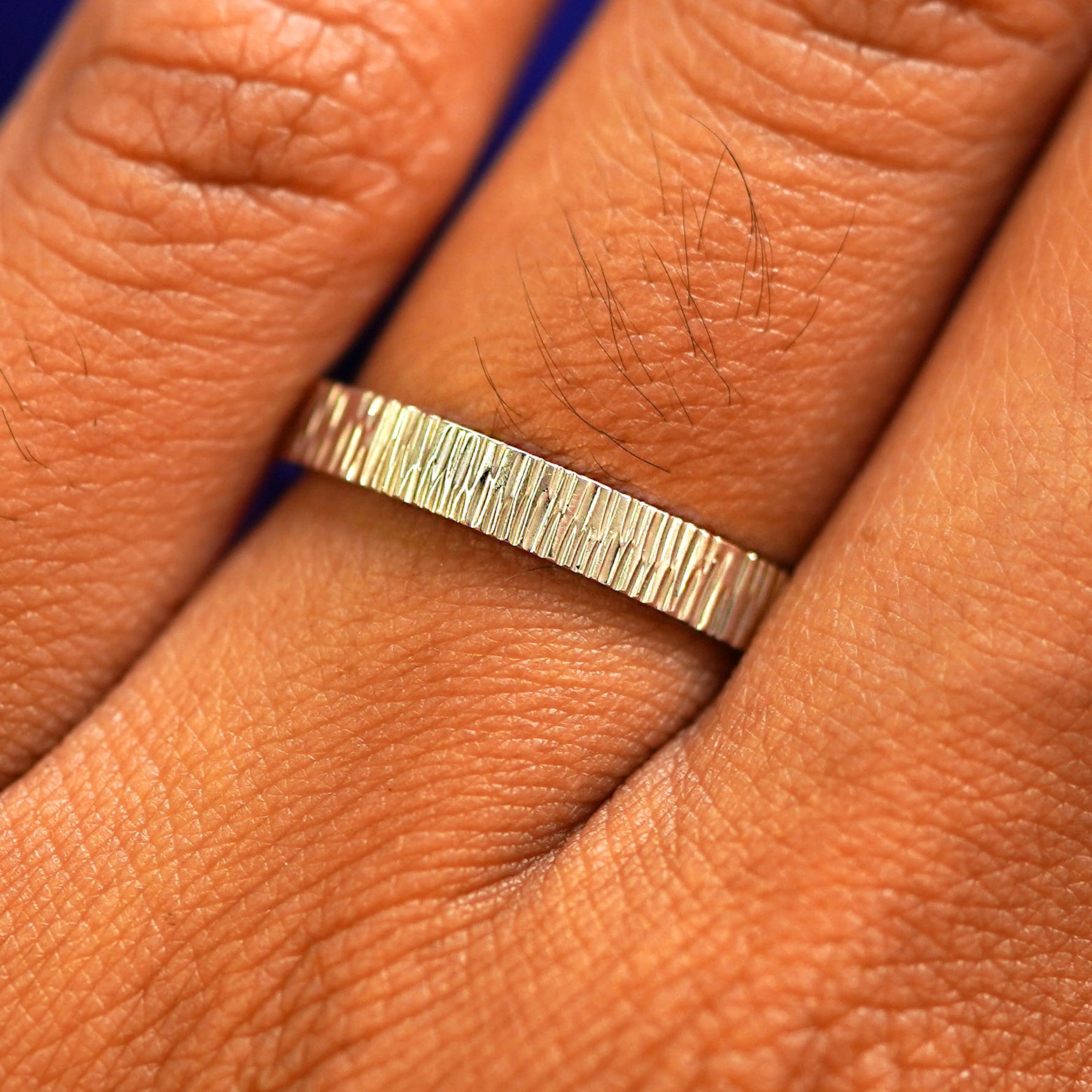 Close up view of a model's fingers wearing a 14k champagne gold Industrial Wood Band