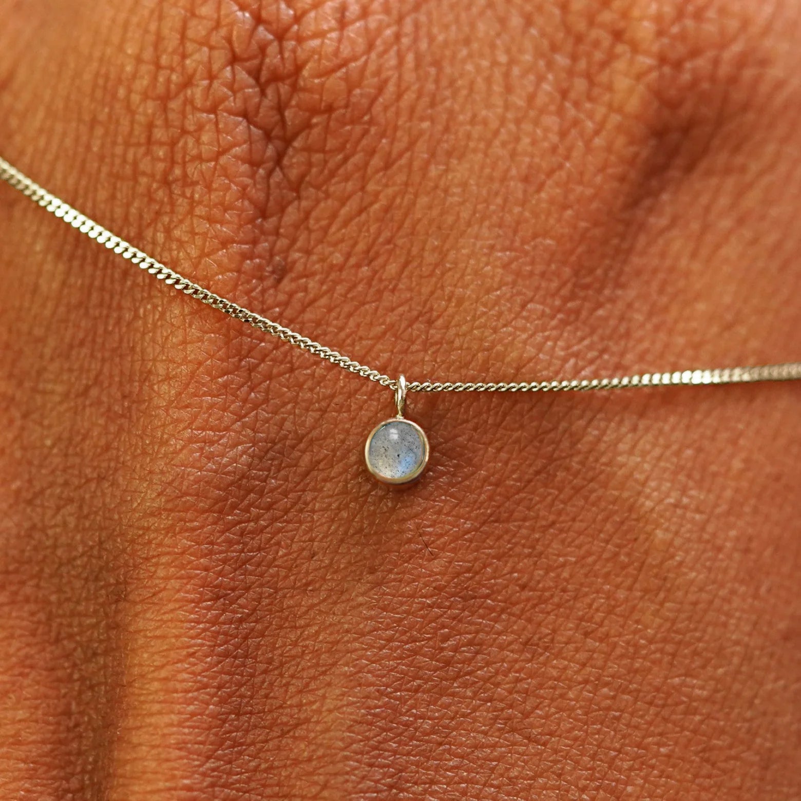 Close up view of a 14k champagne gold Labradorite Necklace draped across the back of a model's hand