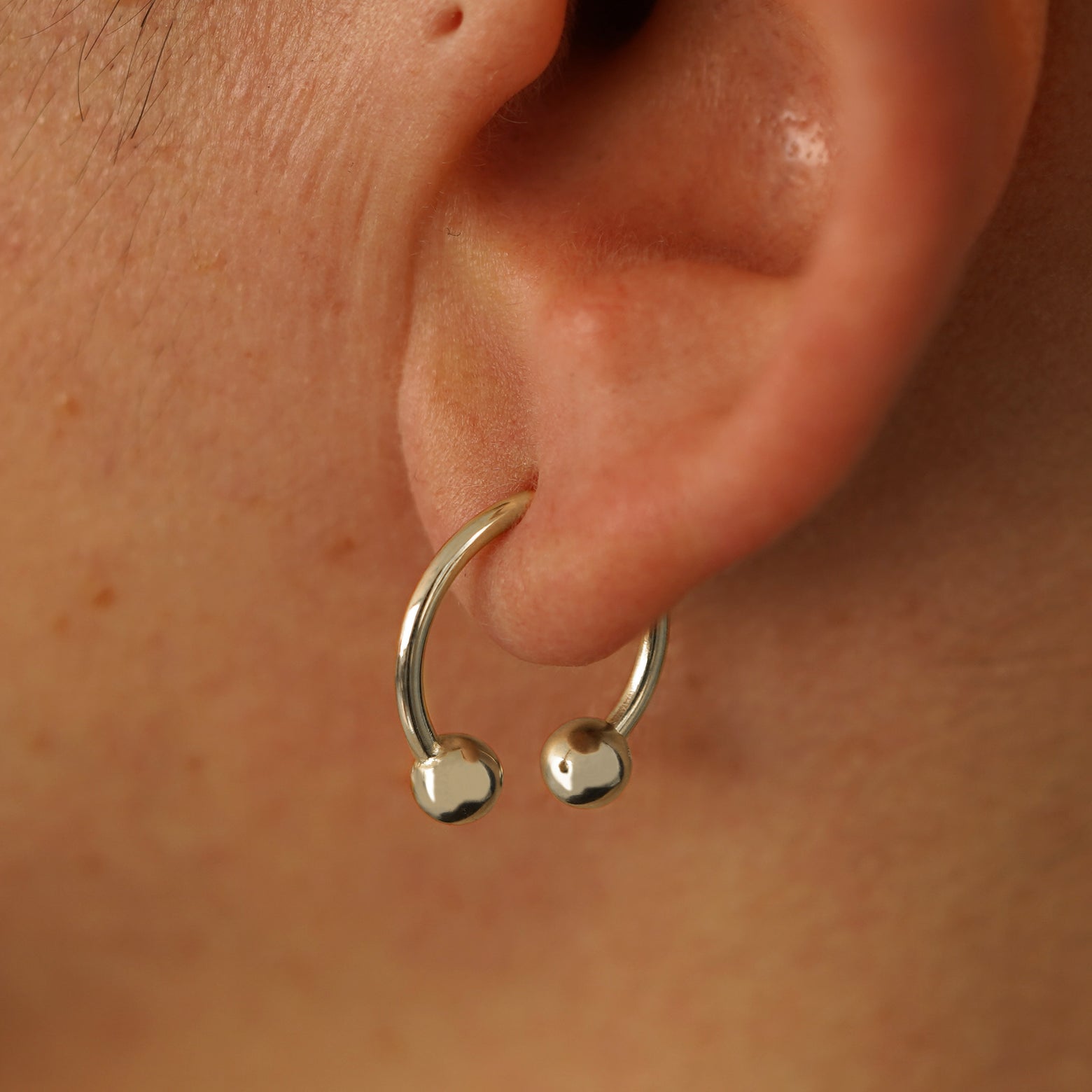 Close up view of a model's ear wearing a 14k champagne gold Large Horseshoe through a lobe piercing