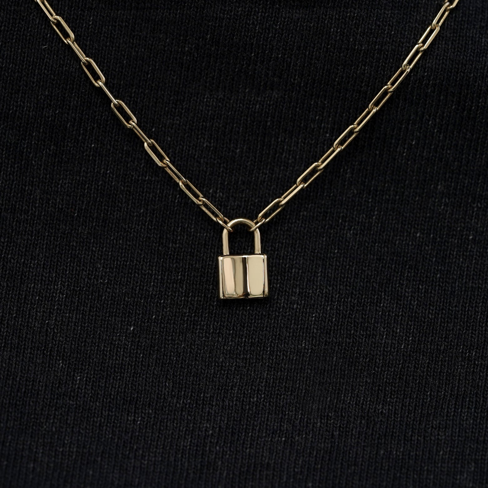 Close up view of a solid 14k champagne gold lock necklace against a model's black shirt