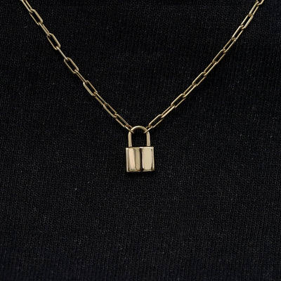 Close up view of a solid 14k champagne gold lock necklace against a model's black shirt