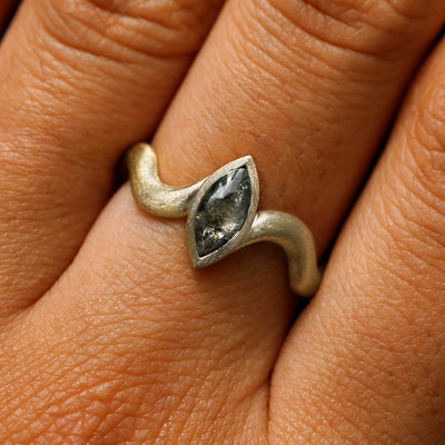 Close up view of a model's hand wearing a 14k champagne gold marquise cabochon salt and pepper diamond engagement ring