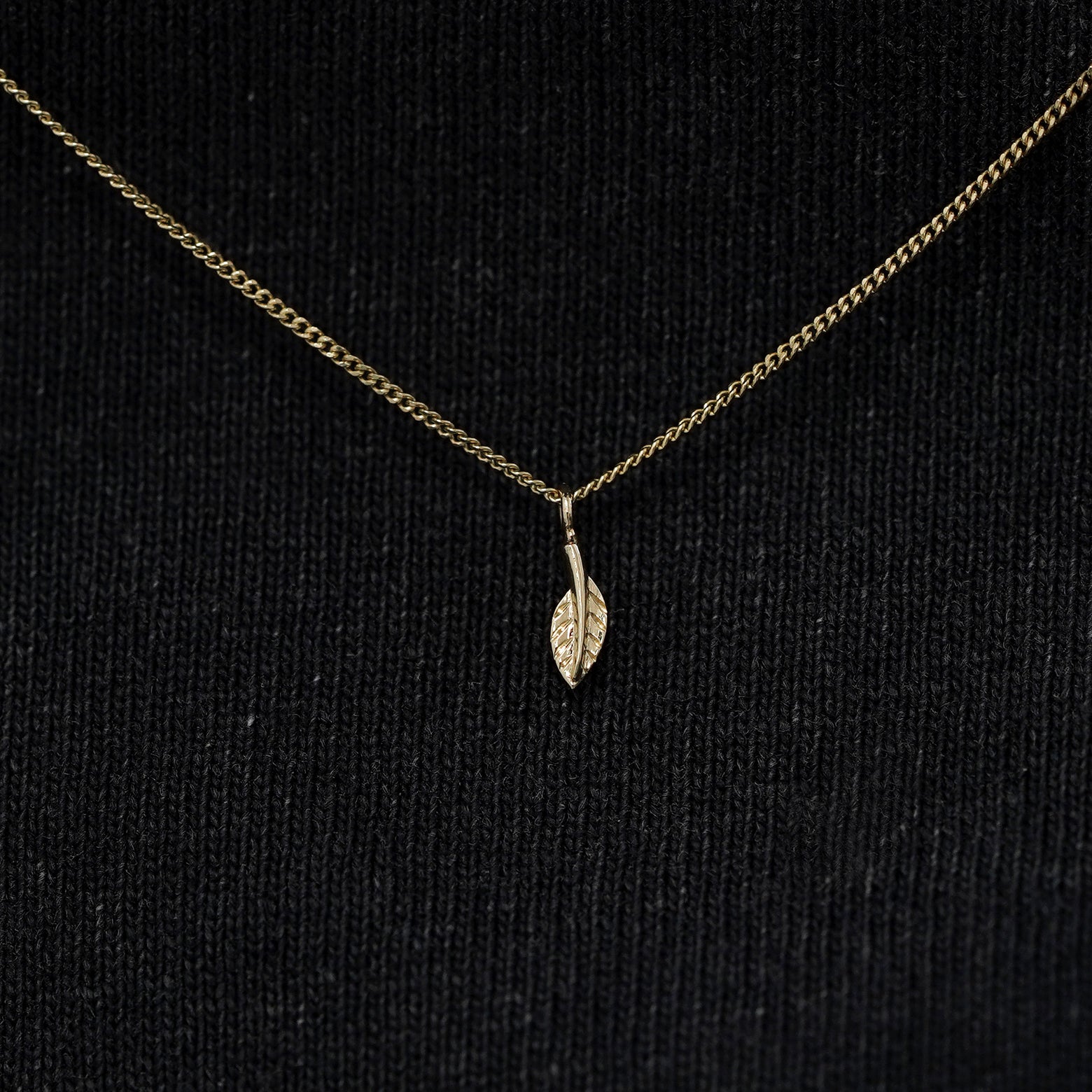 Close up view of a solid 14k champagne gold mini leaf necklace against a model's black shirt