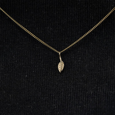 Close up view of a solid 14k champagne gold mini leaf necklace against a model's black shirt