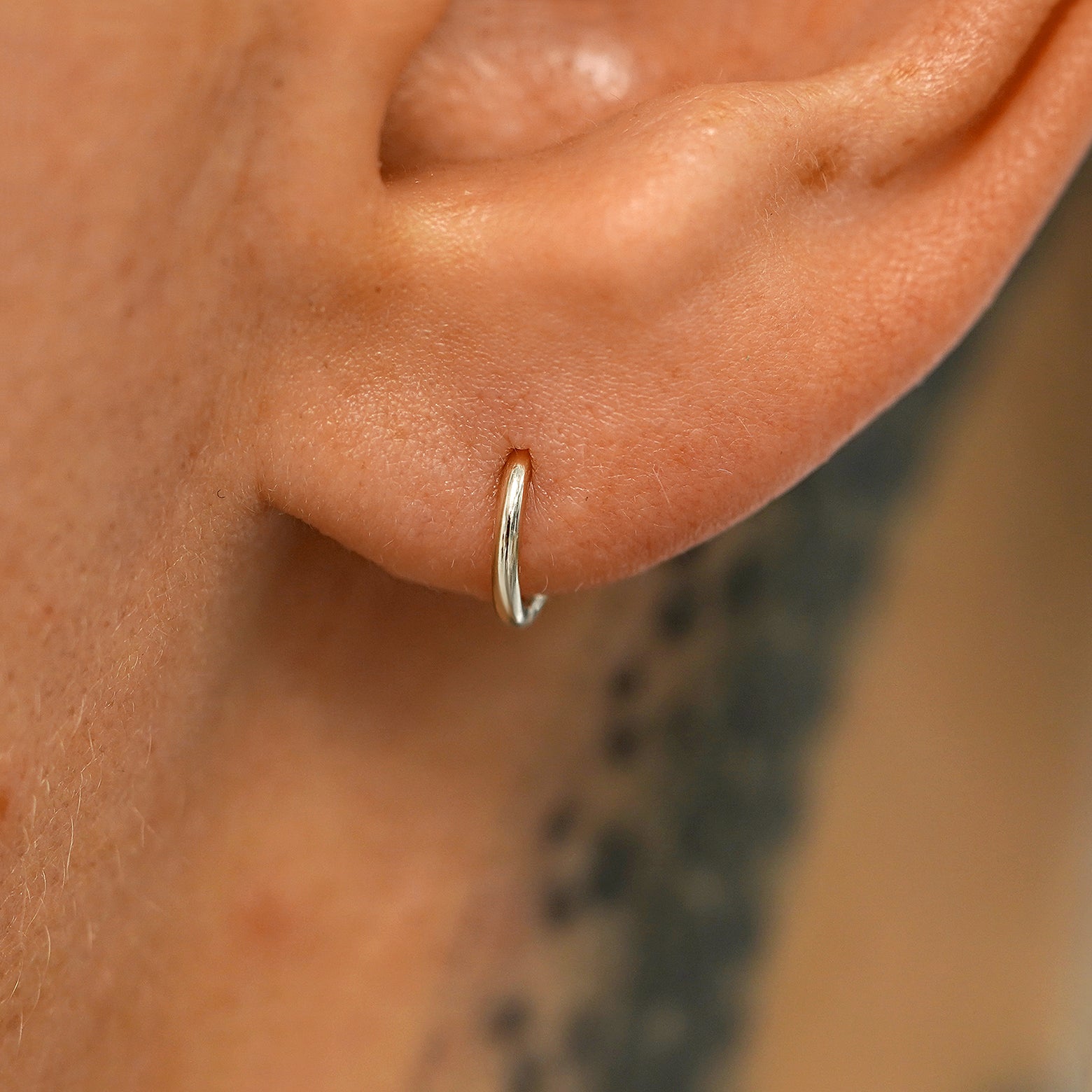 A model's ear wearing a 14k champagne gold Mini Seamless Huggie Hoop / Piercing