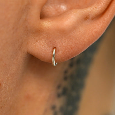 A model's ear wearing a 14k champagne gold Mini Seamless Huggie Hoop / Piercing