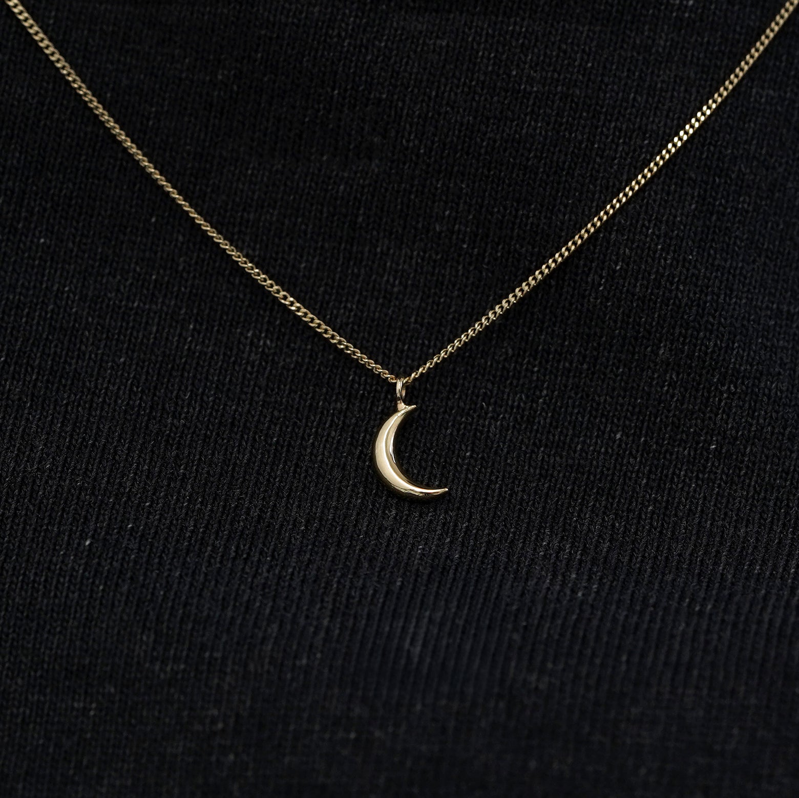 Close up view of a solid 14k champagne gold moon necklace against a model's black shirt