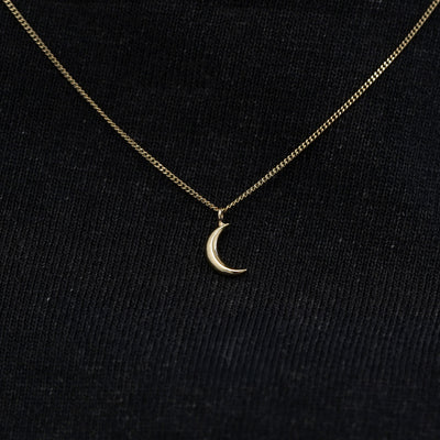 Close up view of a solid 14k champagne gold moon necklace against a model's black shirt