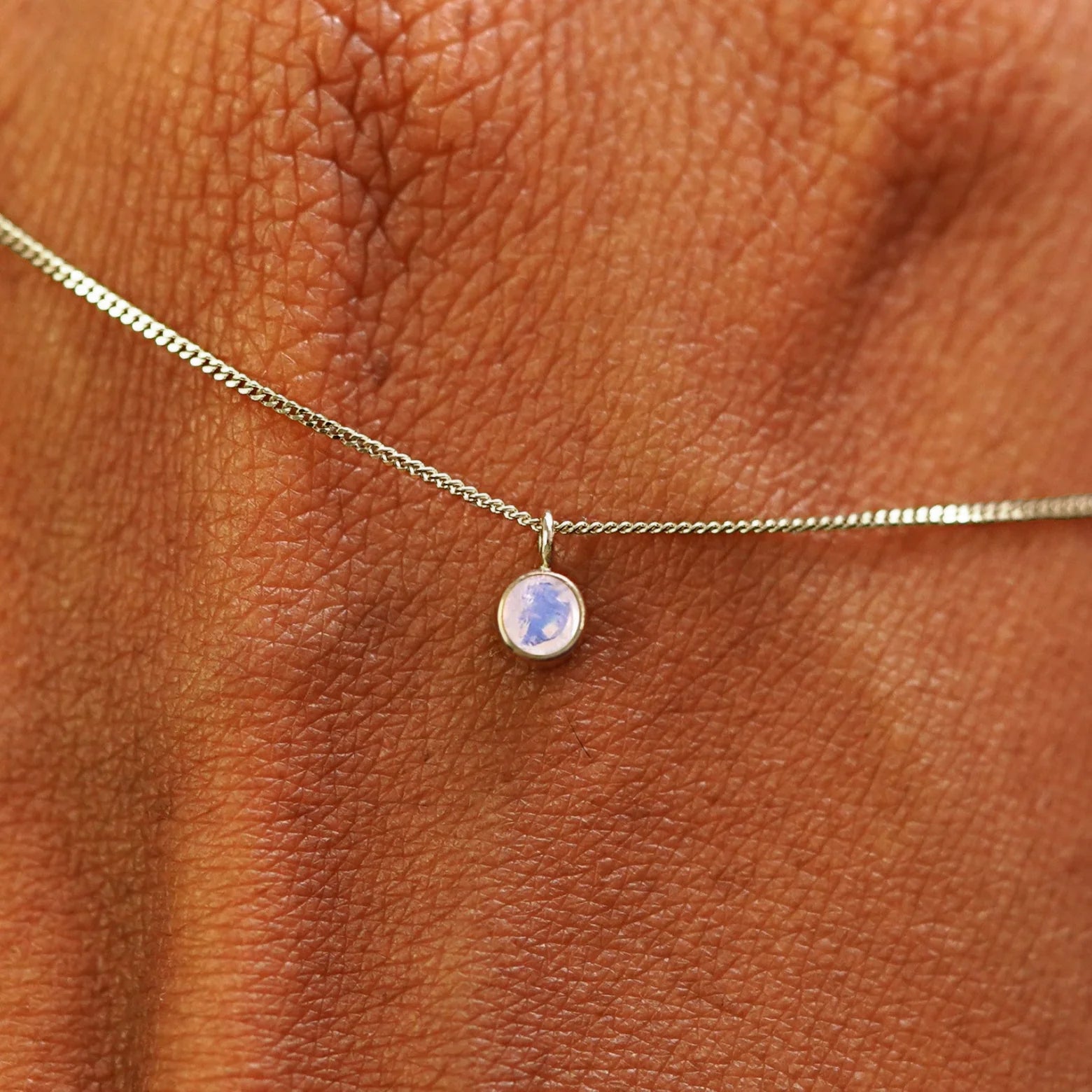 Close up view of a 14k champagne gold Moonstone Necklace draped across the back of a model's hand