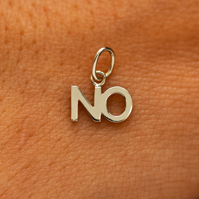 A solid 14k champagne gold No Charm on the back of a models hand