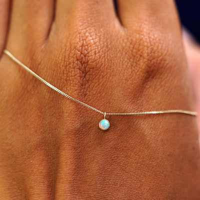 A solid champagne gold Opal Necklace draped across the back of a model's hand
