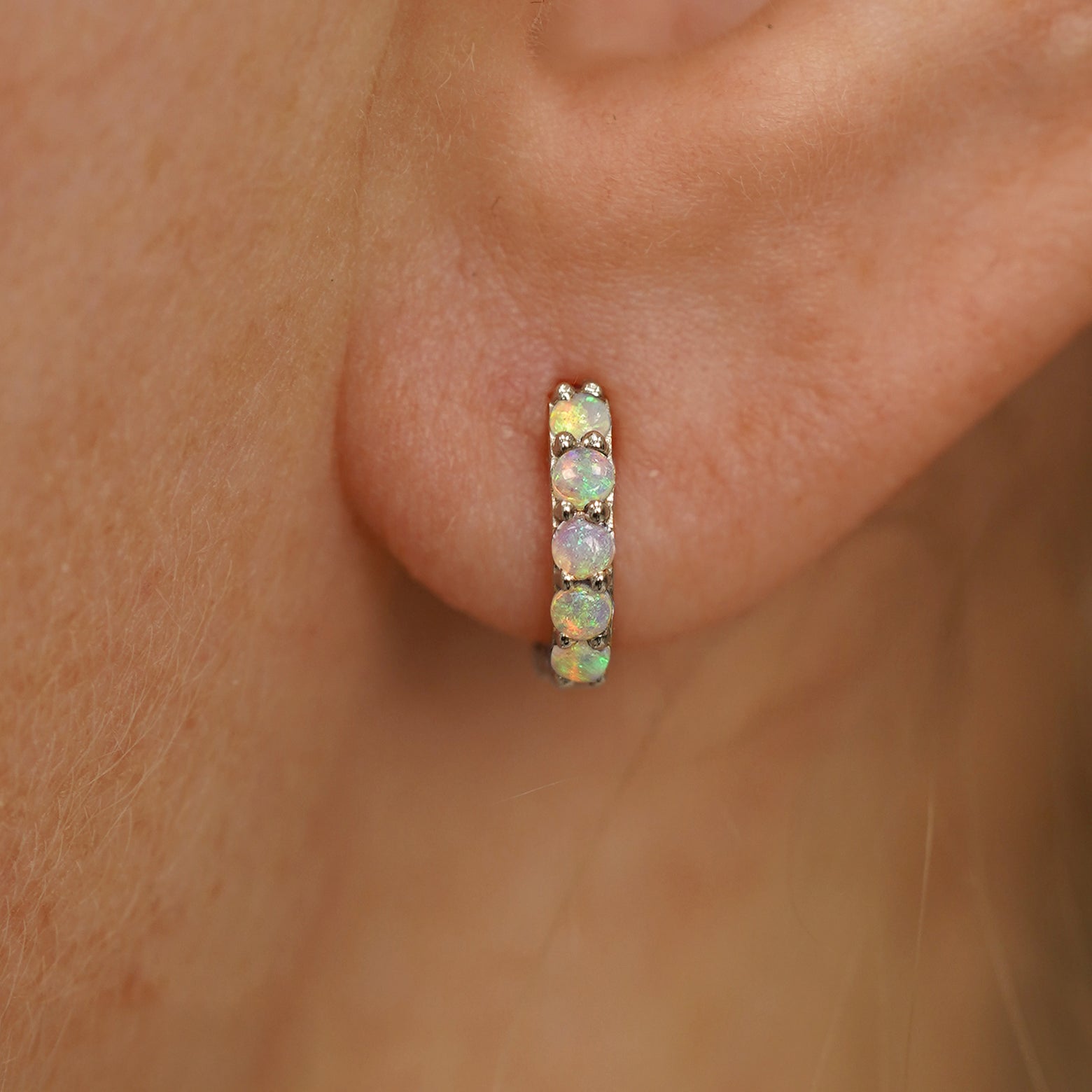 Close up view of a model's ear wearing a champagne gold Mini Opal Huggie Hoop