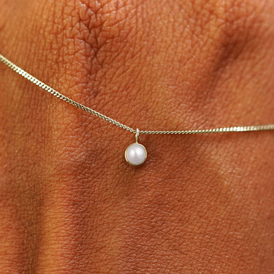 A solid champagne gold Pearl Necklace draped across the back of a model's hand