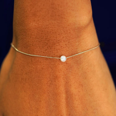 A model's wrist wearing a champagne gold Pearl Slide Bracelet with a 4mm pearl