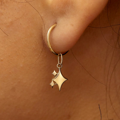 Close up view of a model's ear wearing a champagne gold Sparkly Emoji Charm on a Small Seamless Huggie Hoop
