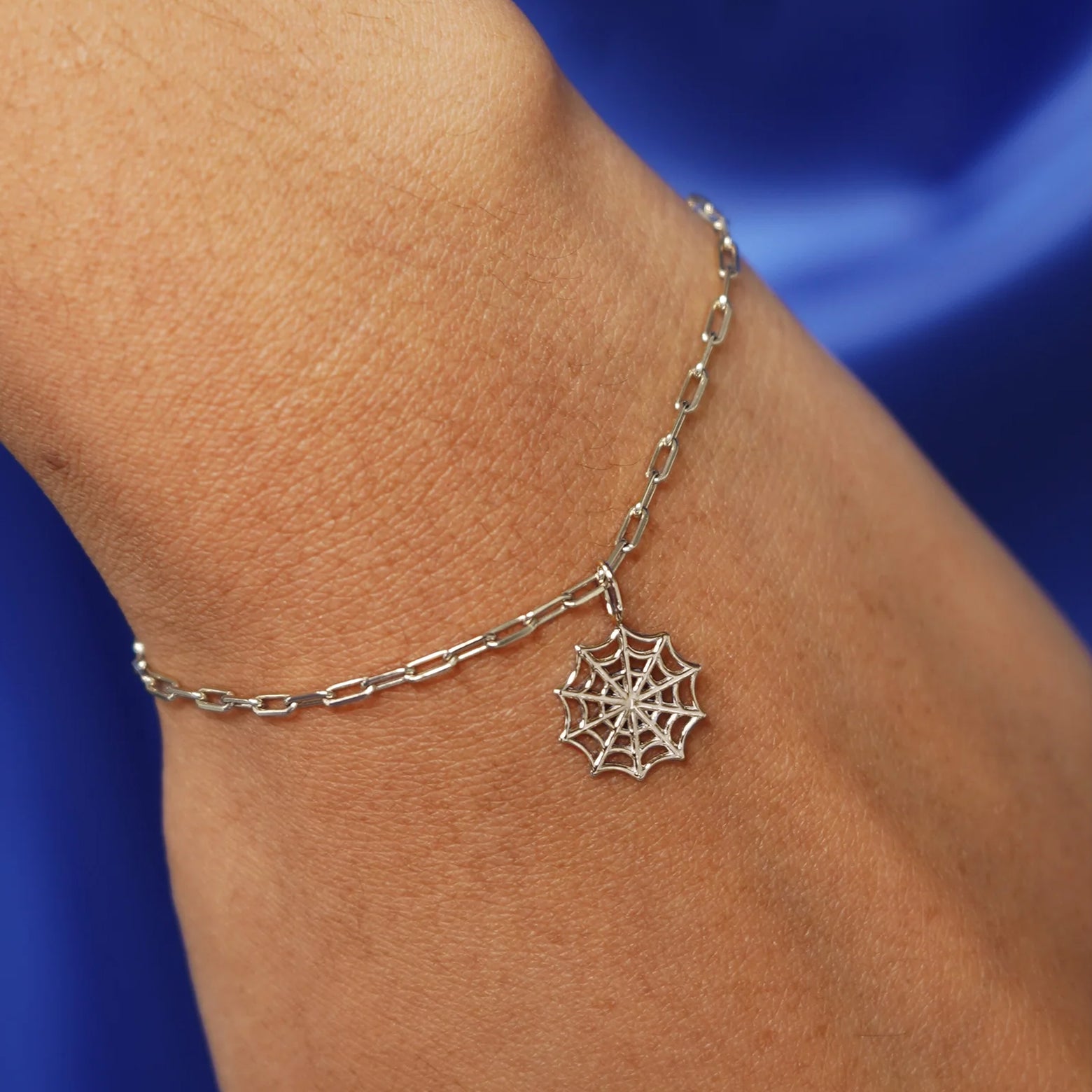 Close up view of a model's wrist wearing a champagne gold Spider Web Charm on a Butch Chain Bracelet