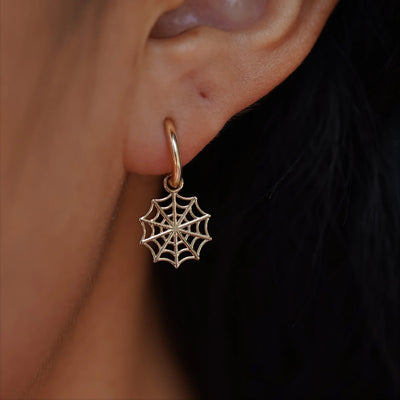 Close up view of a model's ear wearing a champagne gold Spider Web Charm on a Curvy Huggie Hoop