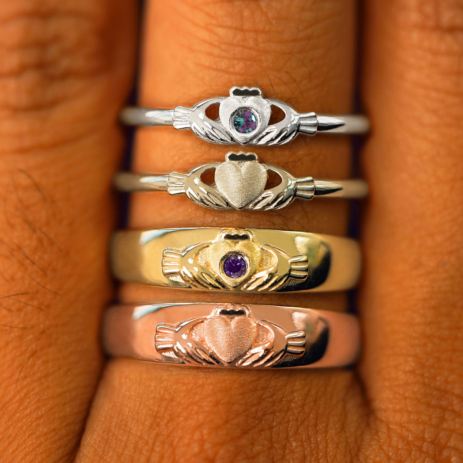 A Claddagh Ring, Gemstone Claddagh Ring, Claddagh Band and Gemstone Claddagh Band stacked in four different gold colors