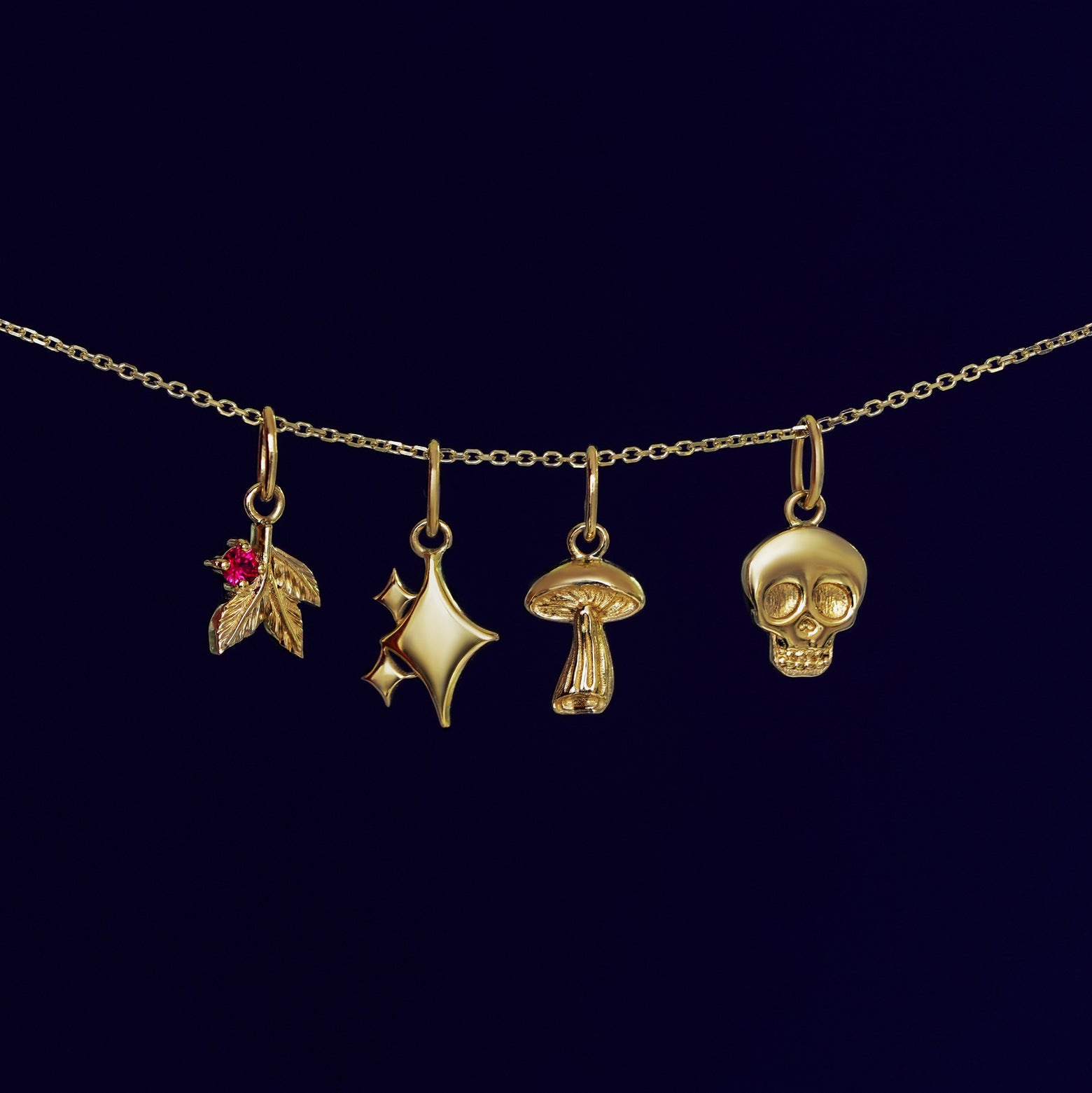 A Gemstone 3 Leaf Charm, Sparkly Emoji Charm, Mushroom Charm, and Skull Charm on a cable chain