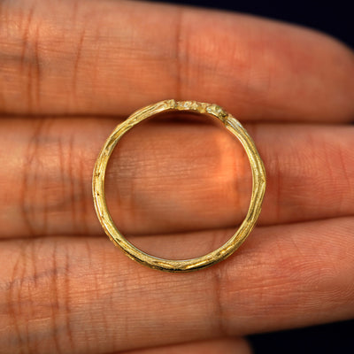 A yellow gold Crashing Waves Band in a model's hand showing the thickness of the band