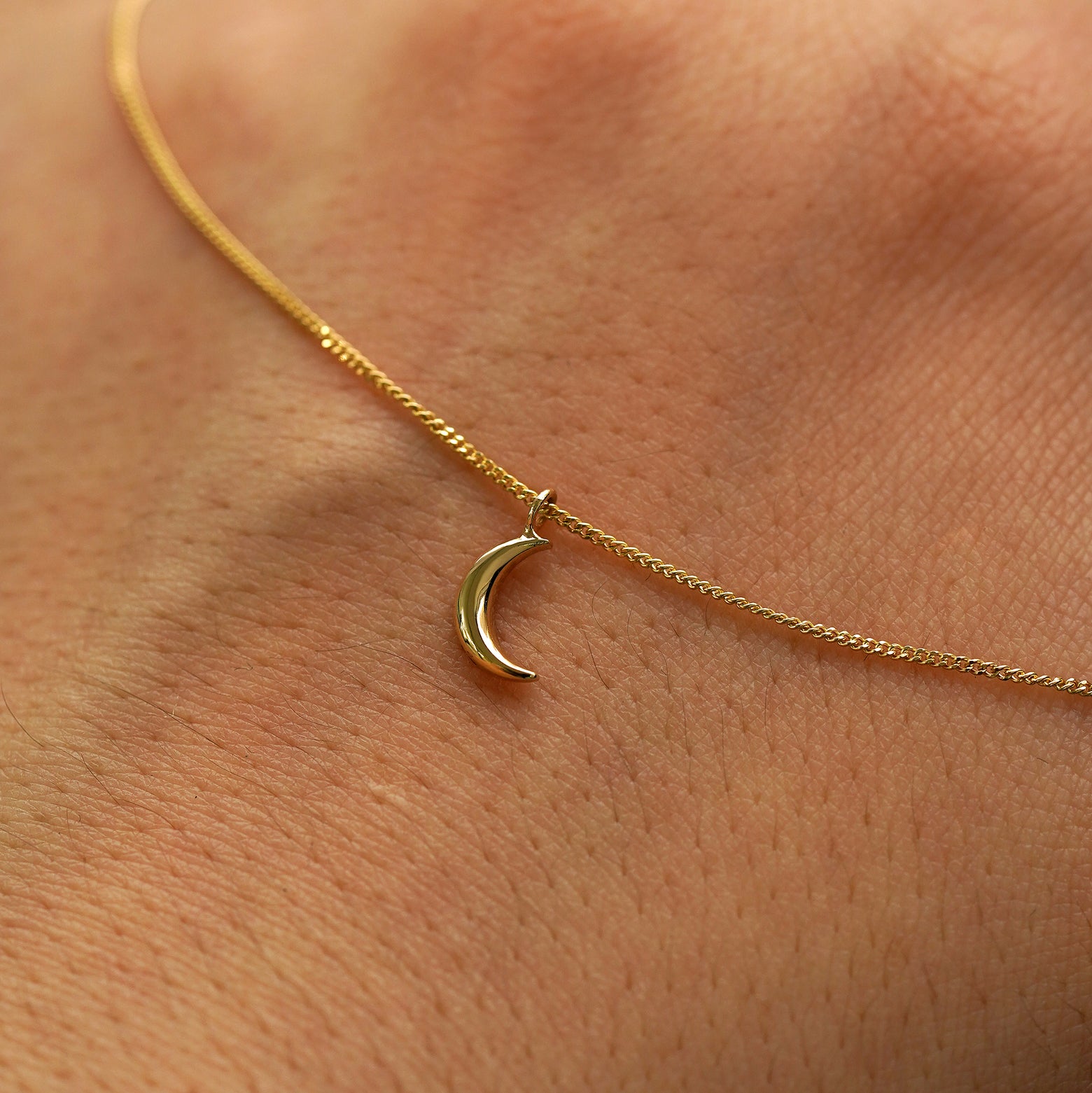 A solid gold crescent moon necklace draped across the back of a model's hand