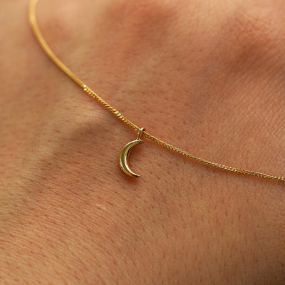 A solid gold crescent moon necklace draped across the back of a model's hand