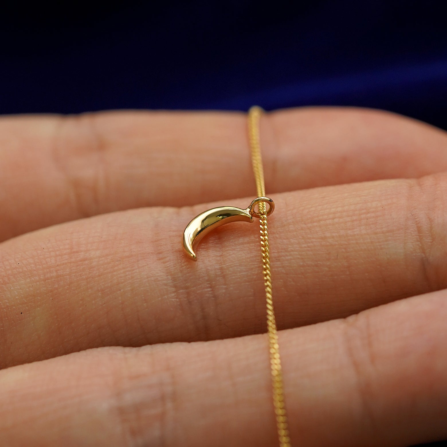 Front side view of a 14k gold moon pendant necklace lying across a model's fingertips
