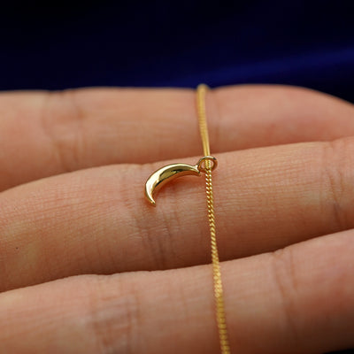 Front side view of a 14k gold moon pendant necklace lying across a model's fingertips