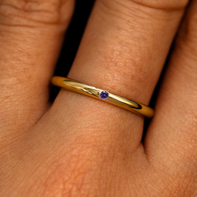 A 14k yellow gold Flush Set Round Purple Sapphire Ring on a model's finger