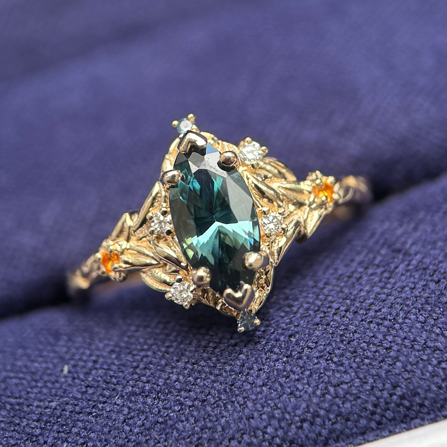 14k Yellow Gold and 1ct Marquise Dark Teal Sapphire with Tiny Round Blue and Orange Sapphires and Lab Diamonds on Leaves Around Gem and Front of the Band Custom Ring, size 4.5