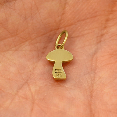Back view of a solid 14k yellow gold Mushroom Charm resting on in the palm of a model's hand