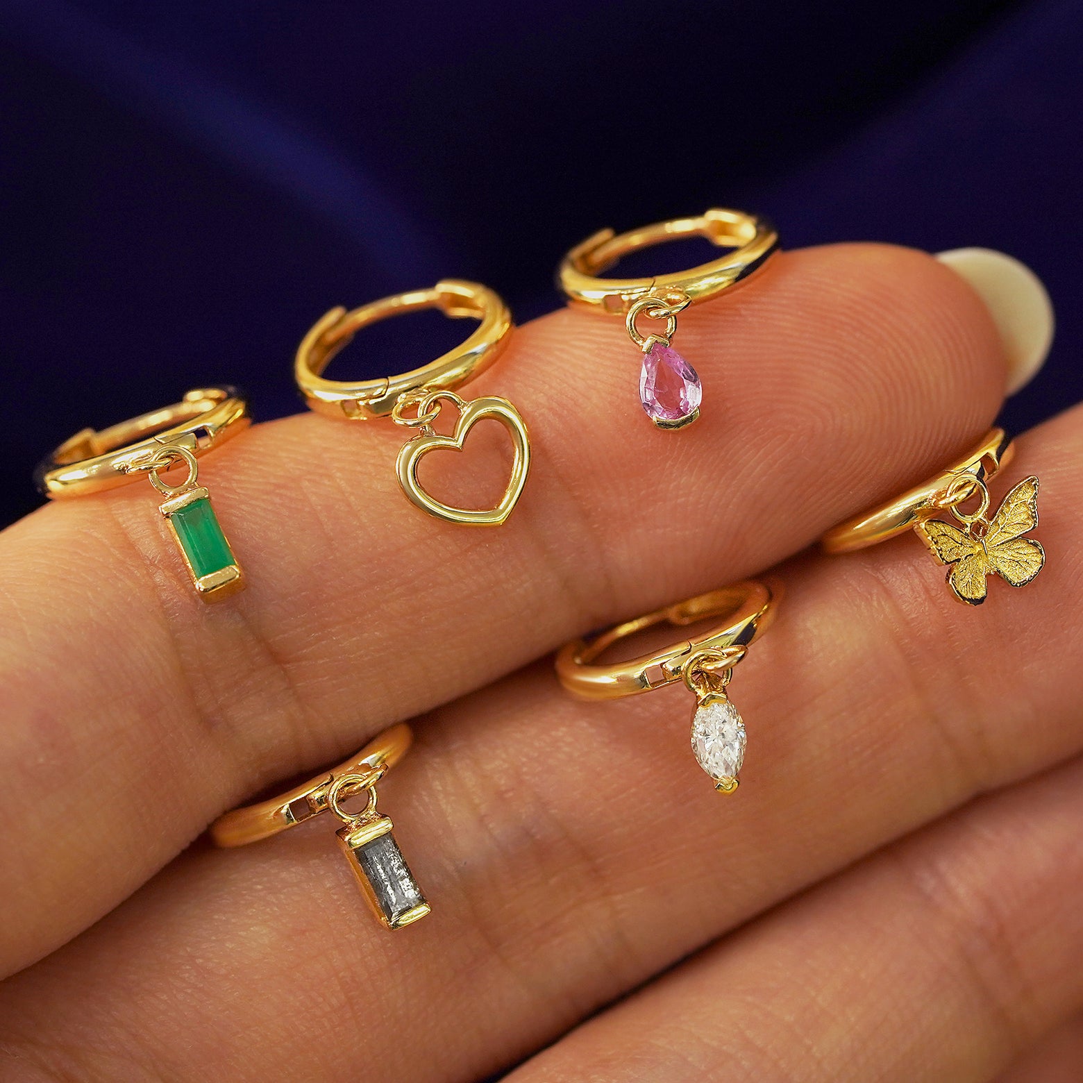 A model balancing six different yellow gold dangle charm hoop earrings on their fingers