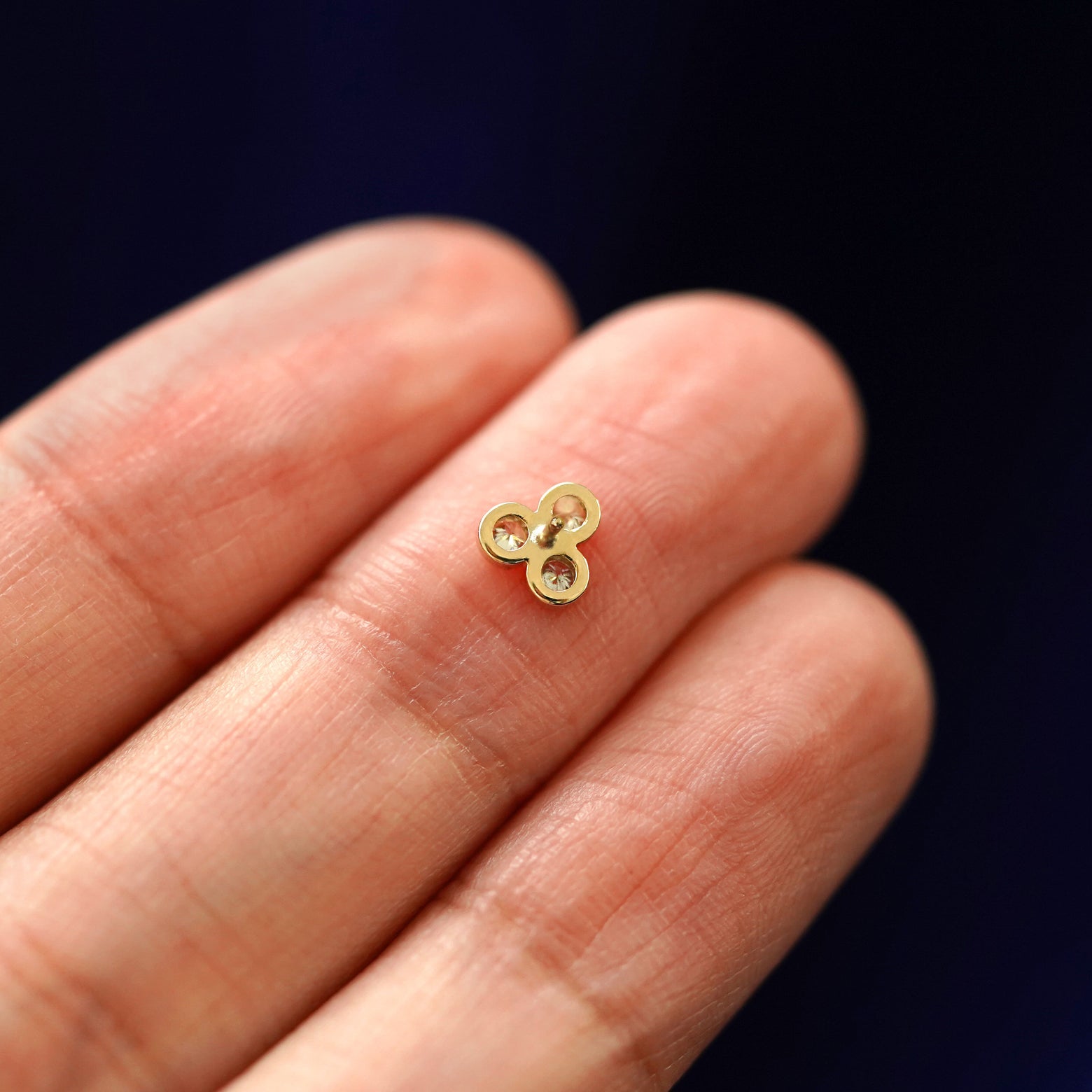A Diamond Trio Earring laying face down on a model's finger tip to show the post without a backing