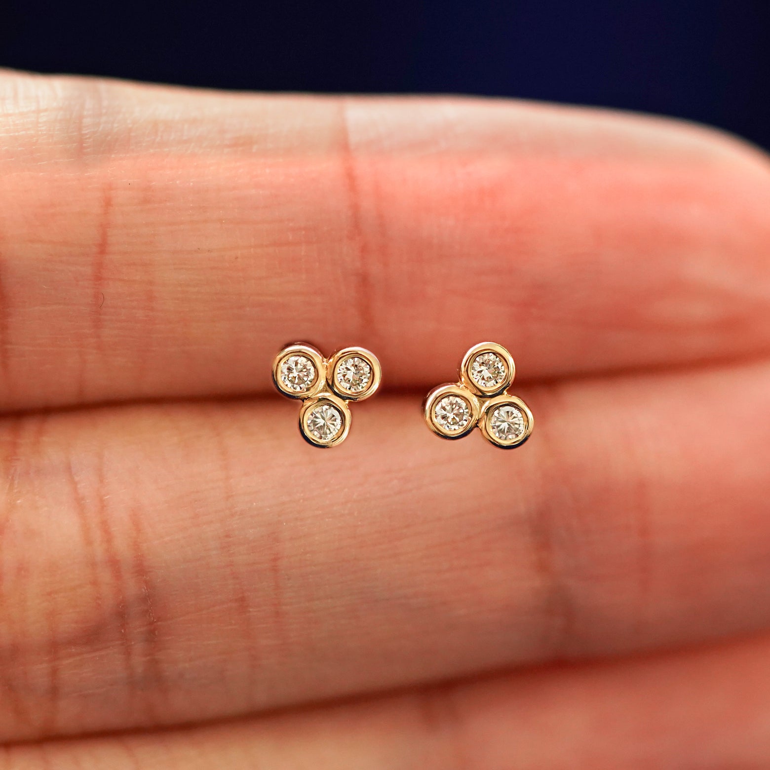 A hand holding a pair of solid yellow gold Diamond Trio stud earrings in between their fingers