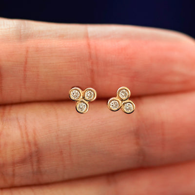 A hand holding a pair of solid yellow gold Diamond Trio stud earrings in between their fingers