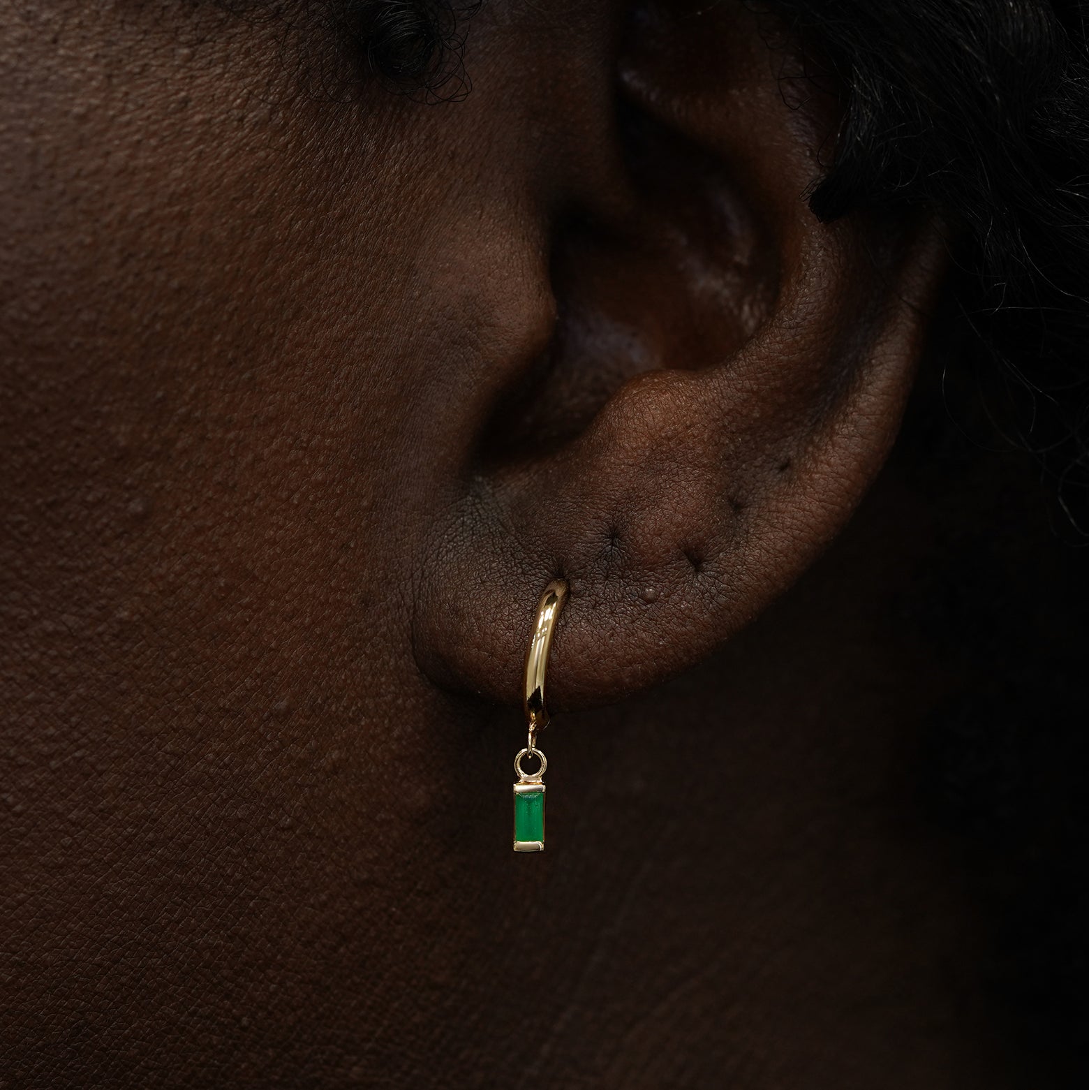 A model wearing a solid 14k gold baguette emerald charm hoop earring