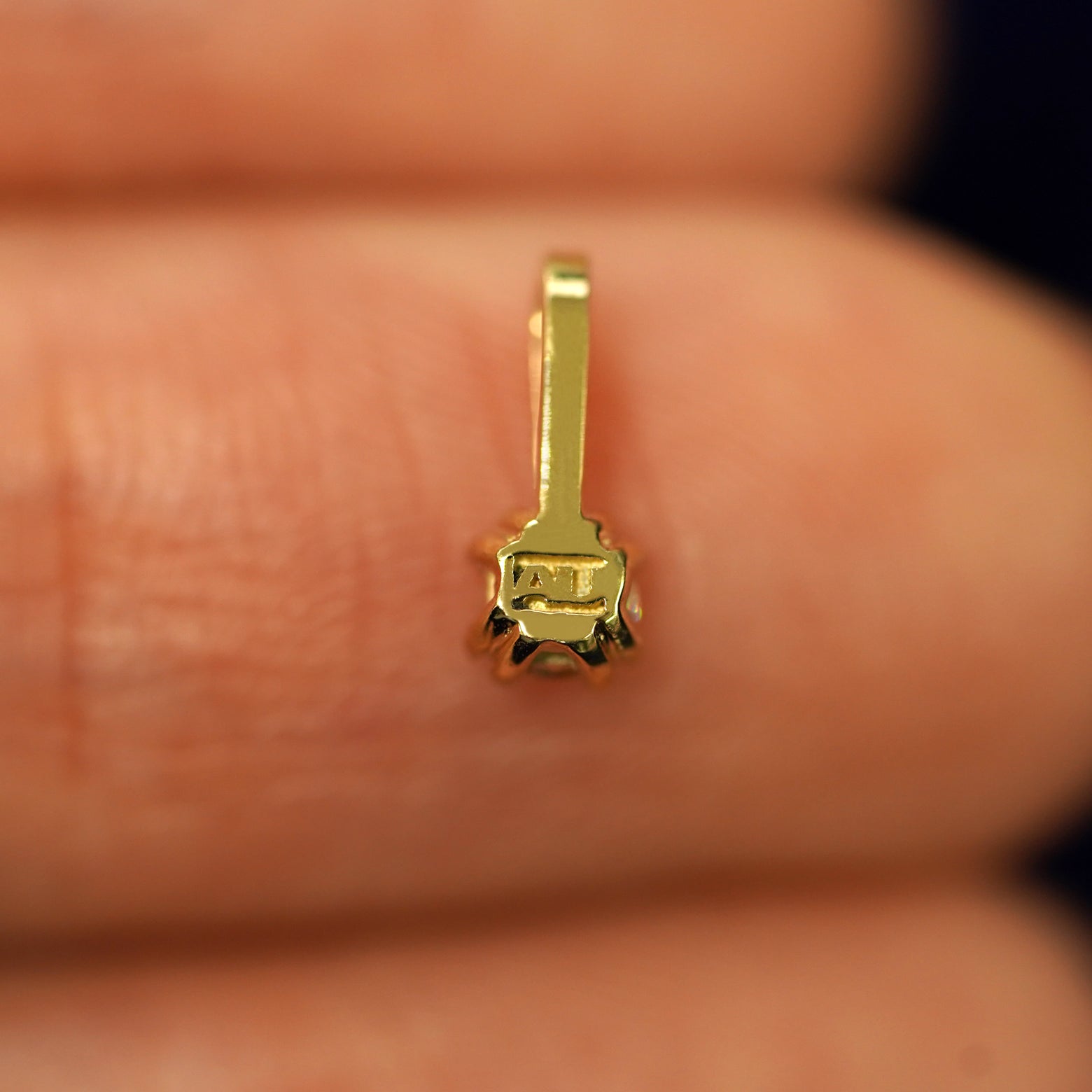 A solid gold Emerald Charm for chain facedown on a model's fingertip to show the solid back of the charm