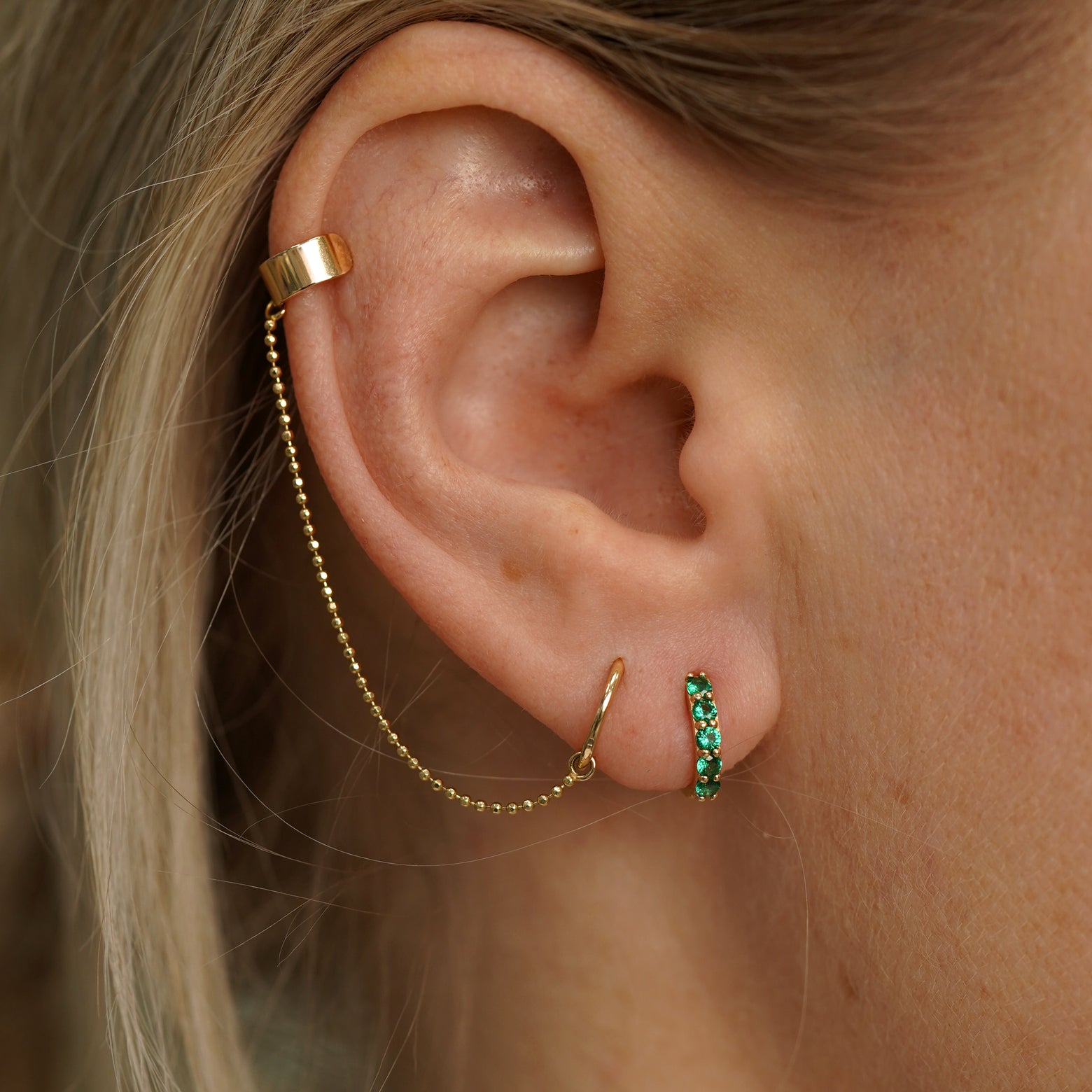 A model wearing a Emerald Huggie Hoop with a Thick Cuff with Chain and Mini Seamless Huggie Hoop