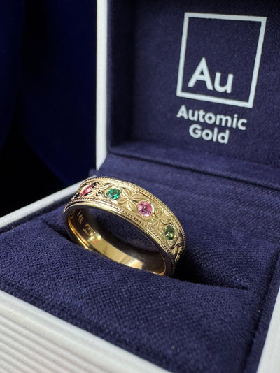 An antique inspired floral milgrain wedding band with round sapphires and emeralds in an Automic Gold ring box