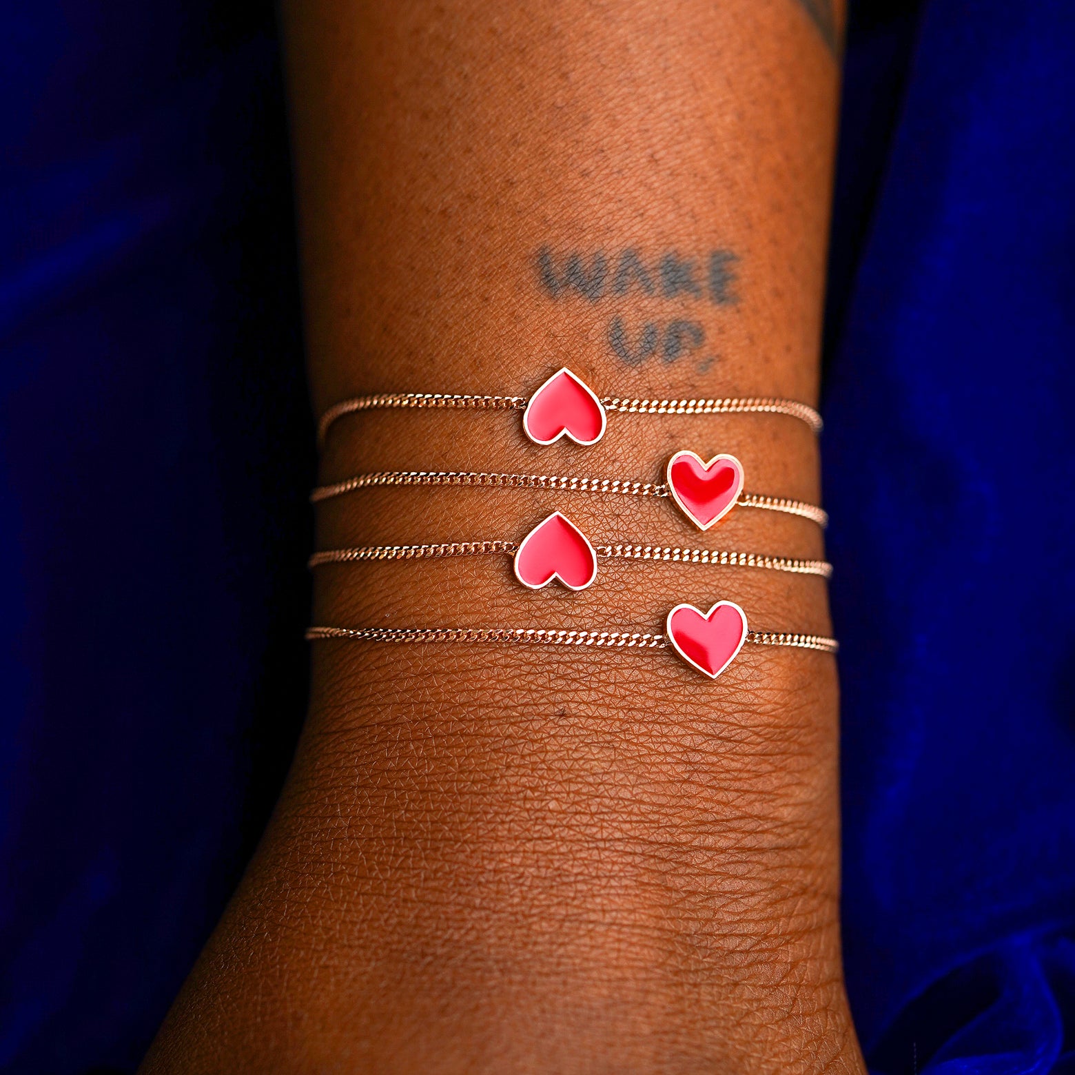 A model's wrist wearing four rose gold red enamel heart bracelet