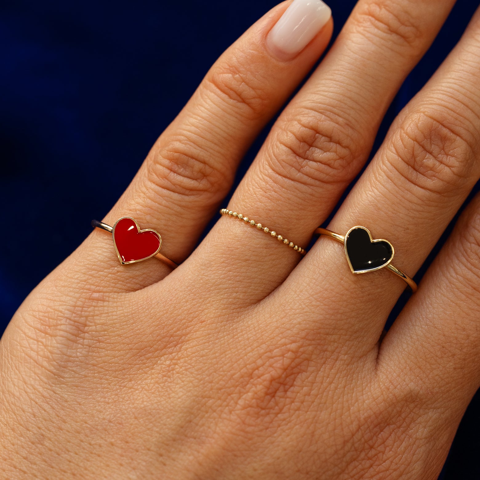 Model is wearing black and red enamel heart rings and bead ring on her fingers