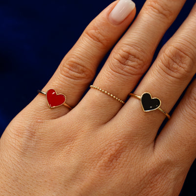 Model is wearing black and red enamel heart rings and bead ring on her fingers