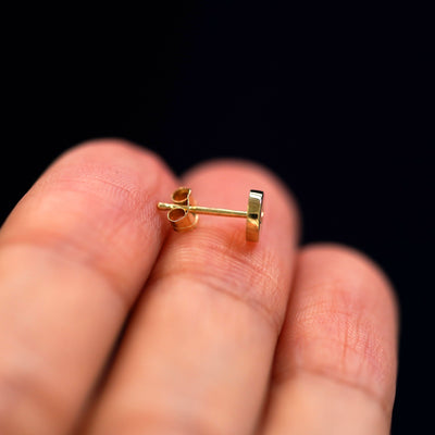 A star disk earring laying flat on a models finger to show the post with a butterfly push back backing on it