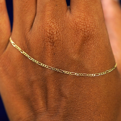 A solid gold Figaro Anklet resting on the back of a model's hand