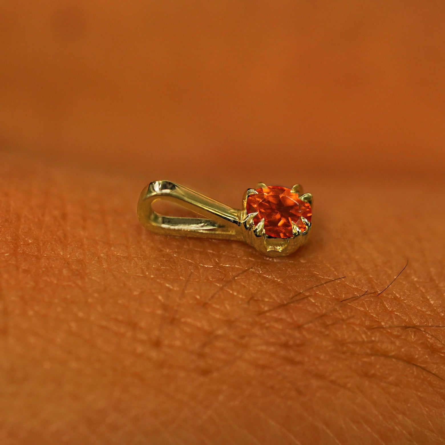 A 14k yellow gold Fire Opal Charm for chain resting on the back of a model's hand