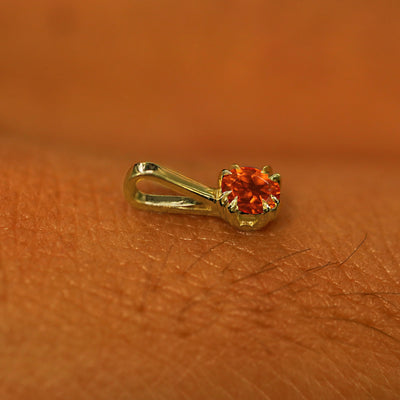 A 14k yellow gold Fire Opal Charm for chain resting on the back of a model's hand