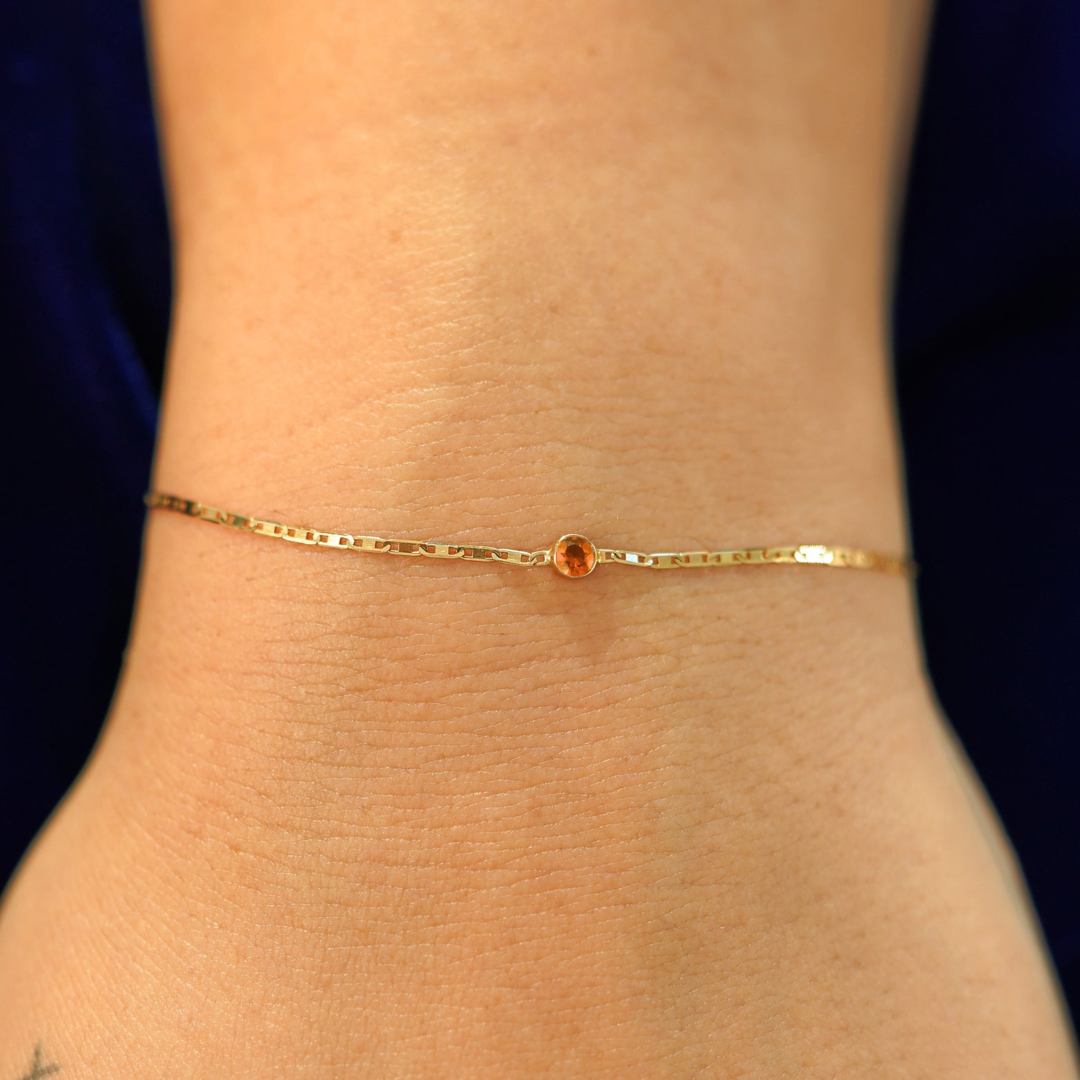 A model's wrist wearing a solid 14k yellow gold Fire Opal Bracelet