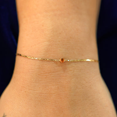 A model's wrist wearing a solid 14k yellow gold Fire Opal Bracelet